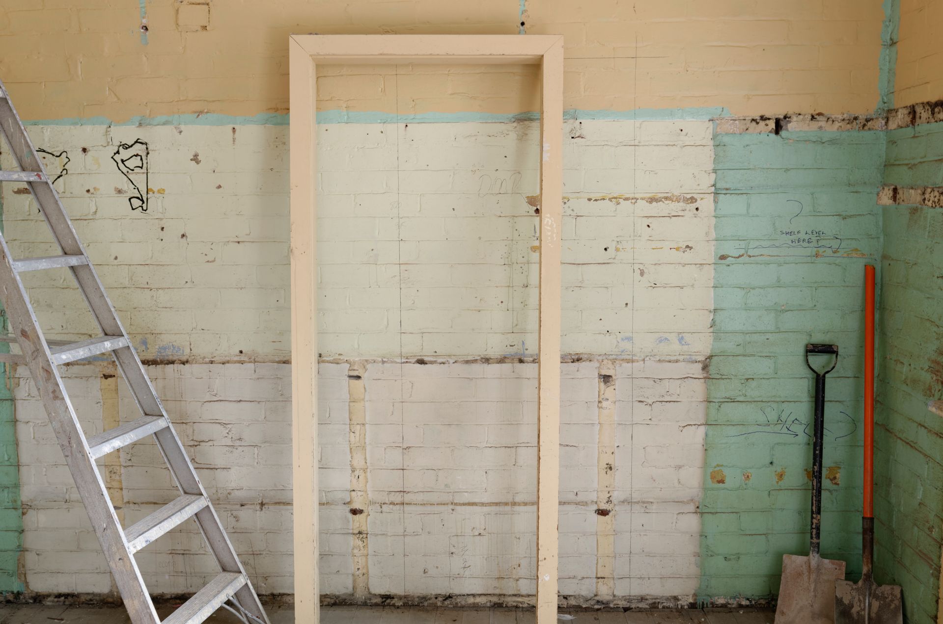Interior demolition site with exposed brick, door frame, ladder, and shovels during a renovation project.